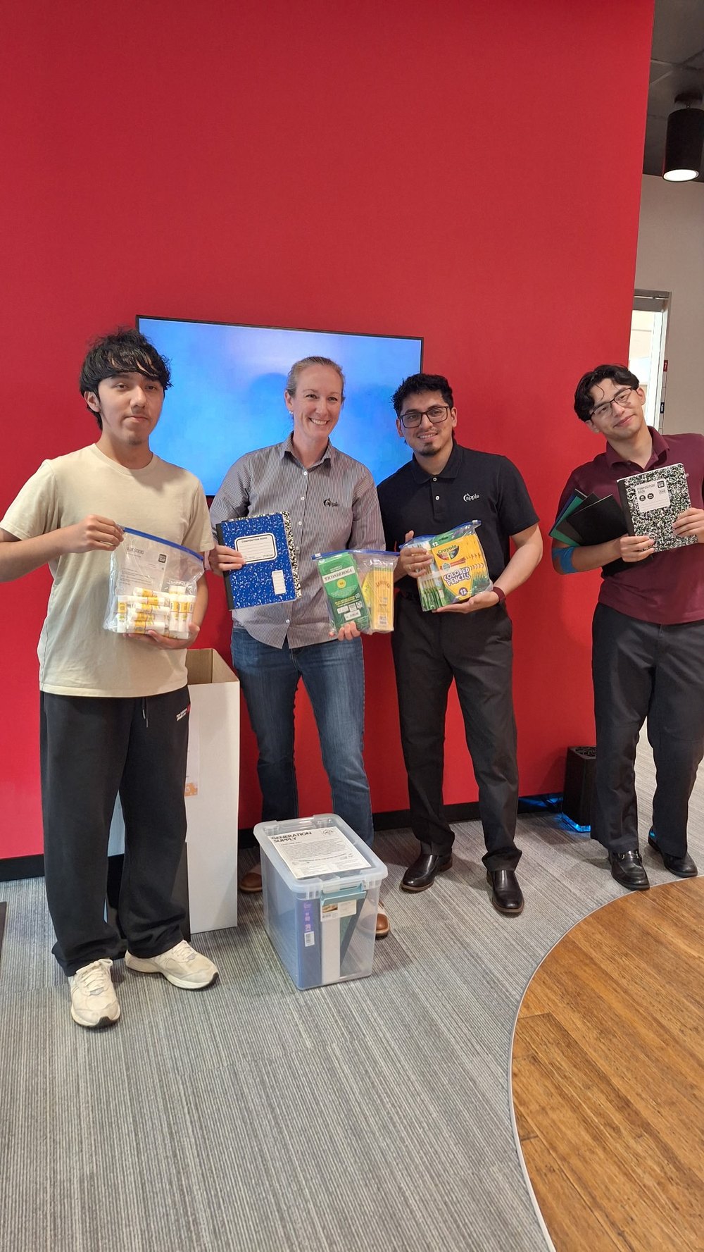 Generation Supply team members with an Apple Federal Credit Union staff member, holding donated school supplies beside a Generation Supply collection bin.