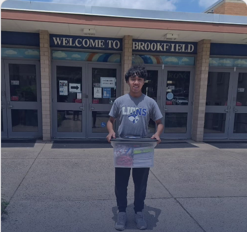 Cesar Carlos standing in front of Brookfield Elementary holding a bin of donated school supplies.