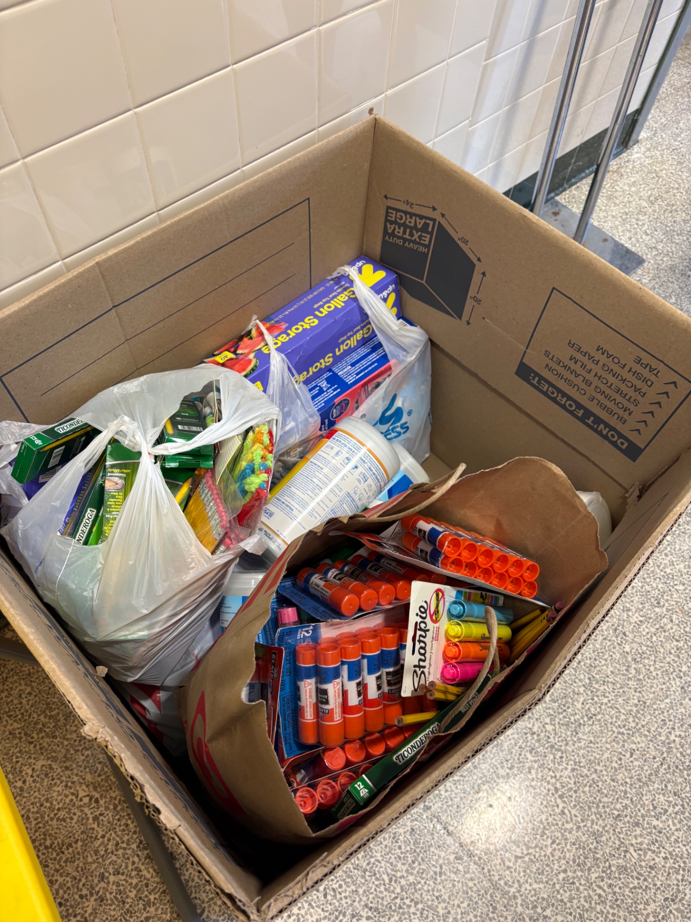 A collection box at Greenbriar East Elementary filled with donated pencils, glue sticks, markers, and other school supplies.