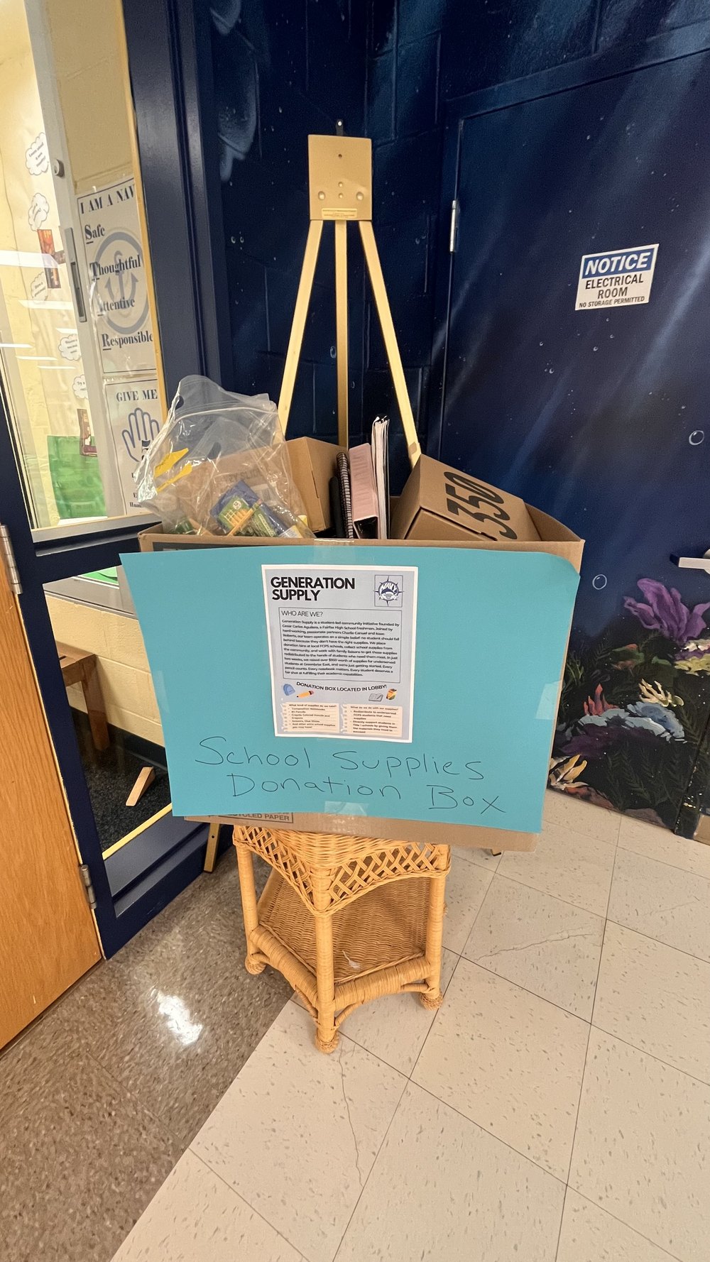 The Generation Supply donation box in the Navy Elementary lobby, filled with donated school supplies beside a hand-lettered sign.