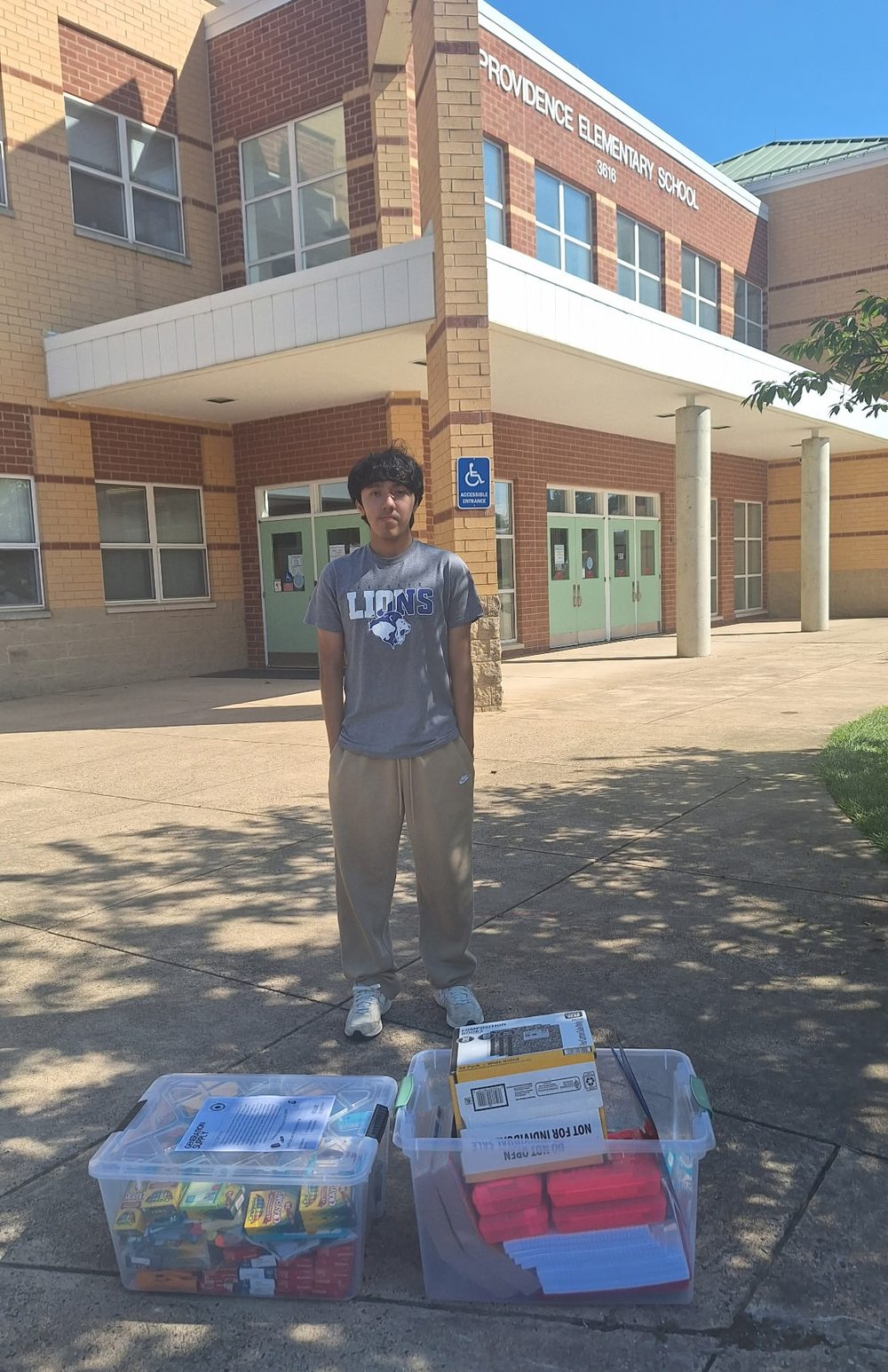 Cesar Carlos outside Providence Elementary School with two bins of donated school supplies.